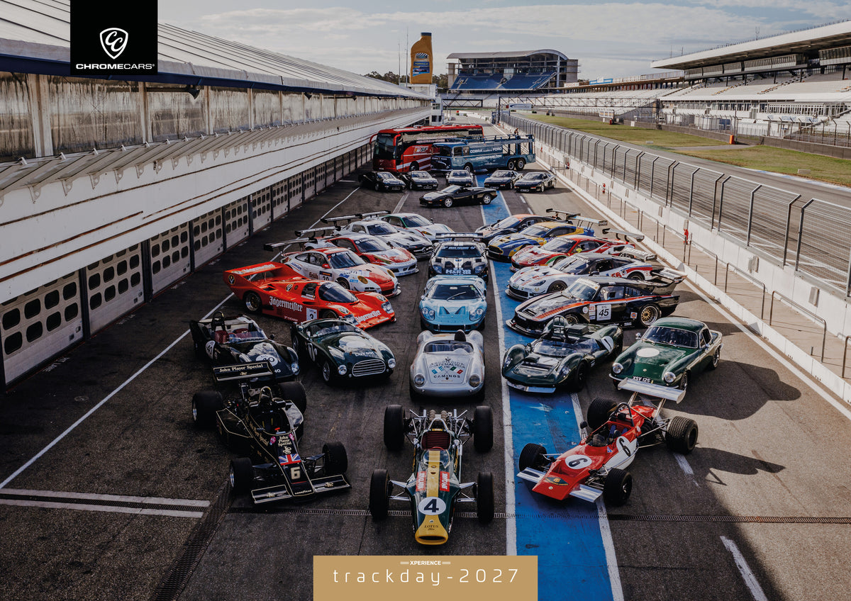 Trackday Kalender 2027 – Deckblatt: Eine große Gruppe unterschiedlicher Rennfahrzeuge steht im Fahrerlager zwischen Boxen und Rennstrecke; die erhöhte Perspektive zeigt die ganze Aufstellung