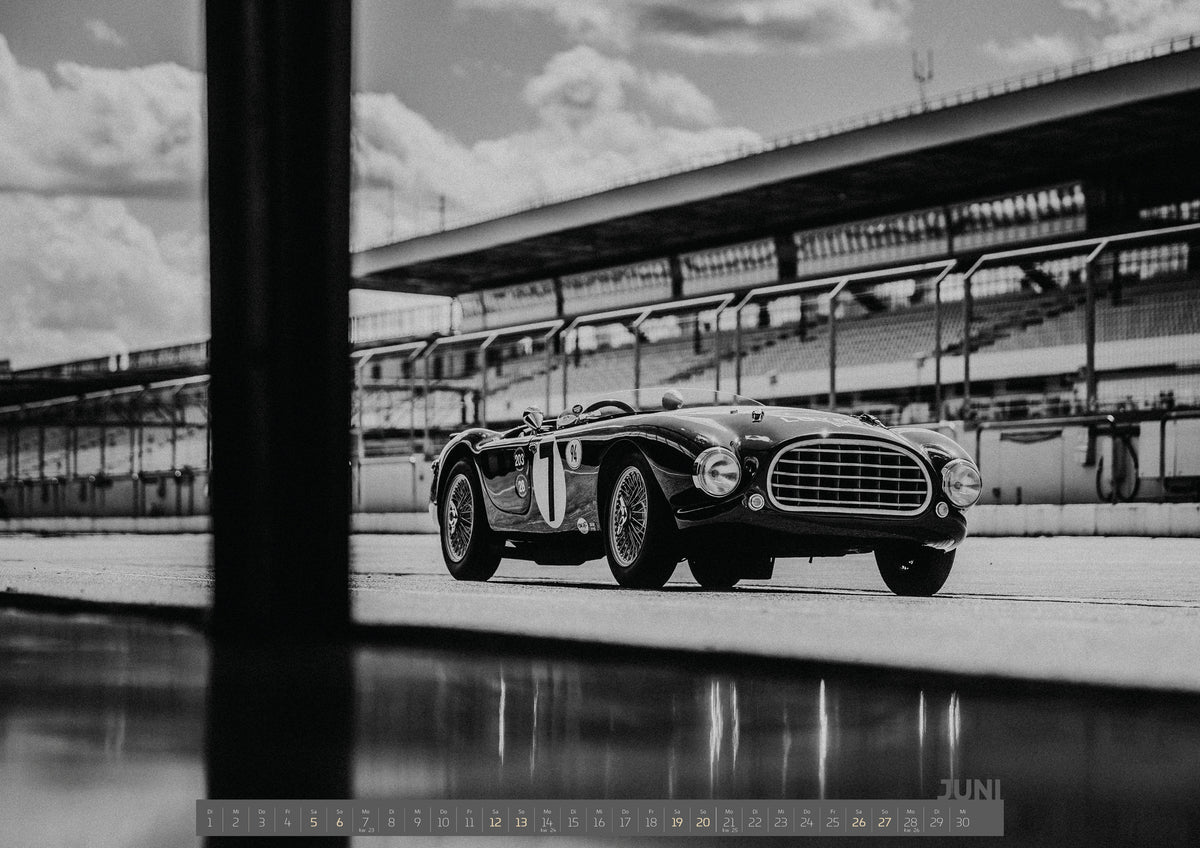 Trackday Kalender 2027 – Juni: Der MG Tojeiro steht im Schwarz-Weiß-Seitenprofil vor der Boxenanlage; sein Spiegelbild erscheint auf dem nassen Boden