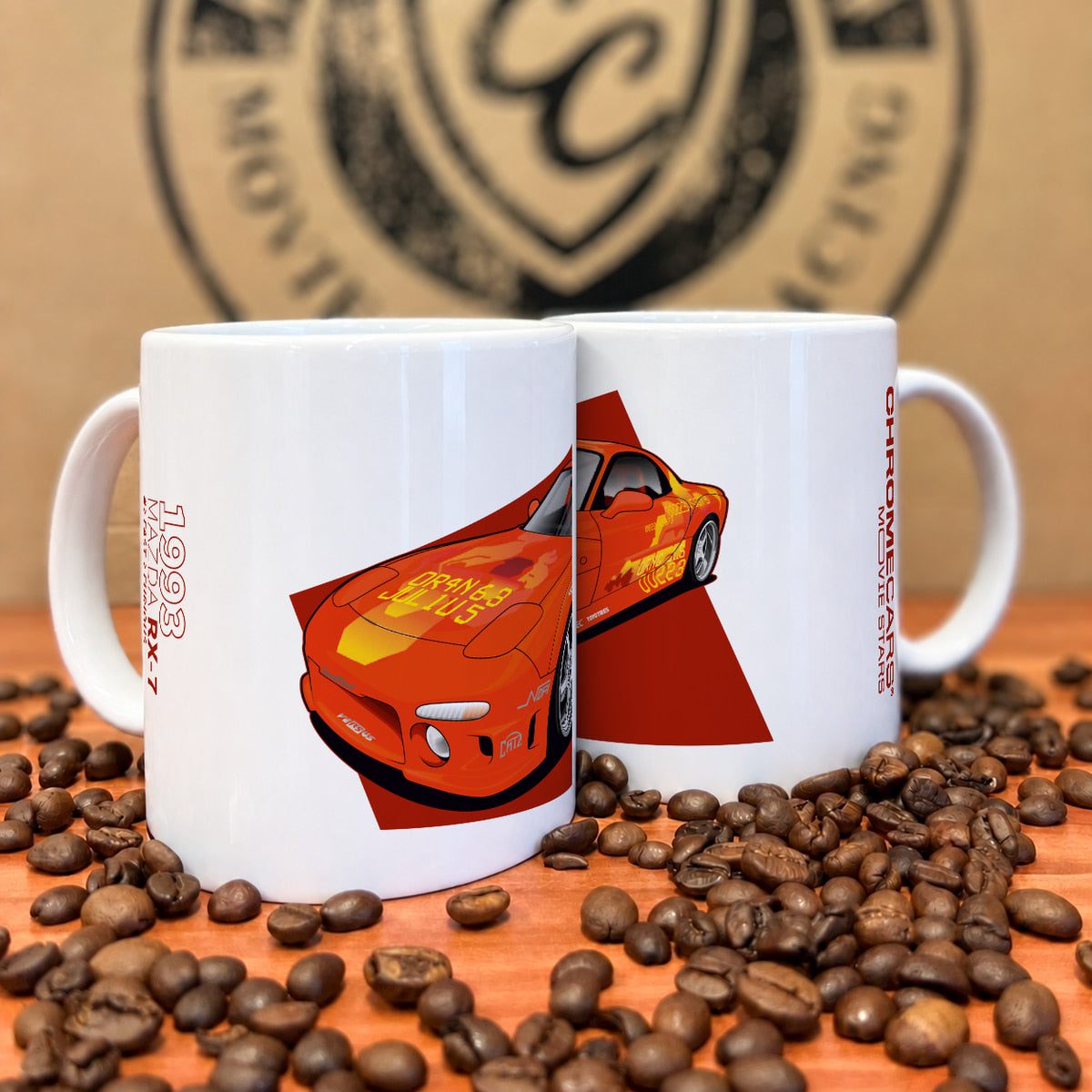 Zwei weiße Tassen mit orangefarbenem Mazda-RX-7-Motiv zwischen Kaffeebohnen.