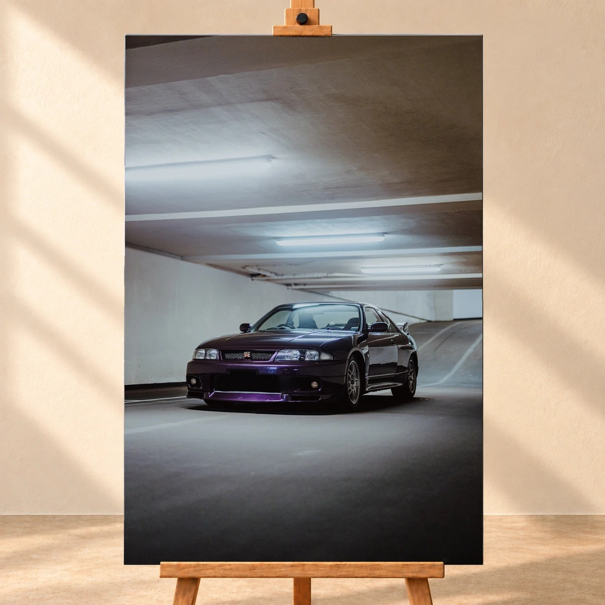 Visualisierung eines hochformatigen Leinwandbildes, frontal auf einer Holzstaffelei vor einer hellen Wand. Das Motiv zeigt einen dunkelvioletten Nissan Skyline GT-R R33 schräg von vorn in einer Tiefgarage.