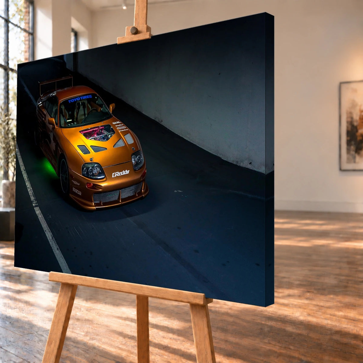 Schrägansicht eines Leinwandbilds als Produktvisualisierung auf einer Holzstaffelei, mit deutlich sichtbarer rechter Seitenkante. Abgebildet ist der orangefarbene Toyota Supra aus „2 Fast 2 Furious“ mit einem Sichtfenster in der Motorhaube und grünem Licht unter dem Wagen.