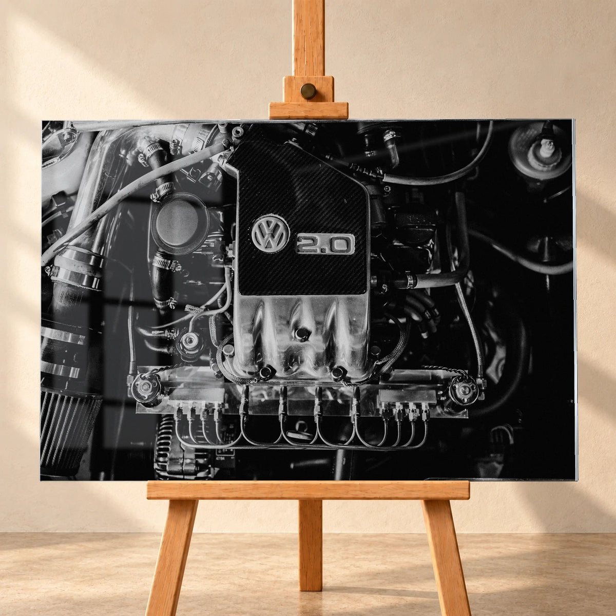 Frontal visualisiertes Acrylglasbild auf einer Holzstaffelei vor heller Wand. Über dem Schwarz-Weiß-Motiv des Motorraums von Jesses VW Jetta mit VW-Emblem und „2.0“ sind Fensterreflexionen sichtbar.