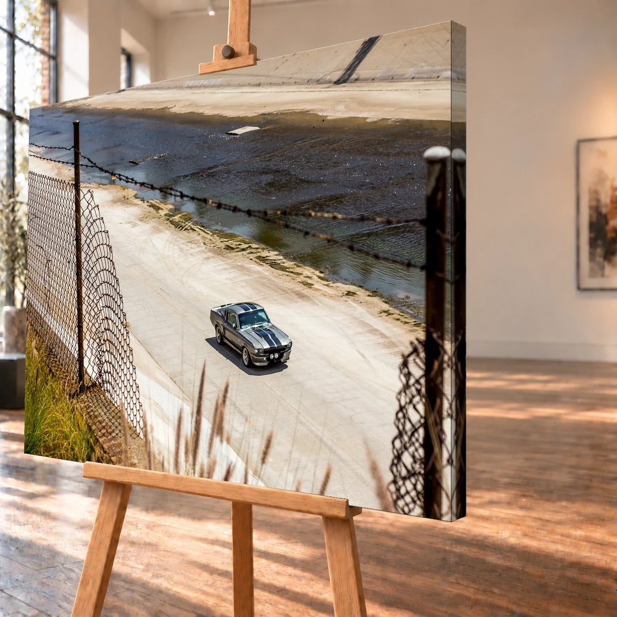 Schrägansicht eines visualisierten Leinwandbilds auf einer Holzstaffelei, mit sichtbar um die rechte Seitenkante fortgeführtem Motiv. Zu sehen ist der silbergraue Ford Mustang Shelby GT500 „Eleanor“ im Betonkanal mit Drahtzaun im Vordergrund.