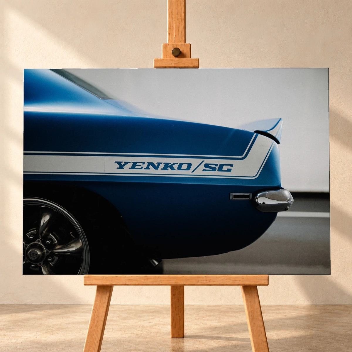 Visualisierung eines Leinwandbilds im Querformat auf einer Holzstaffelei vor heller Wand. Das Motiv zeigt die blaue Heckpartie eines Chevrolet Camaro Yenko mit weißem „YENKO/SC“-Seitenstreifen und Chromstoßstange.