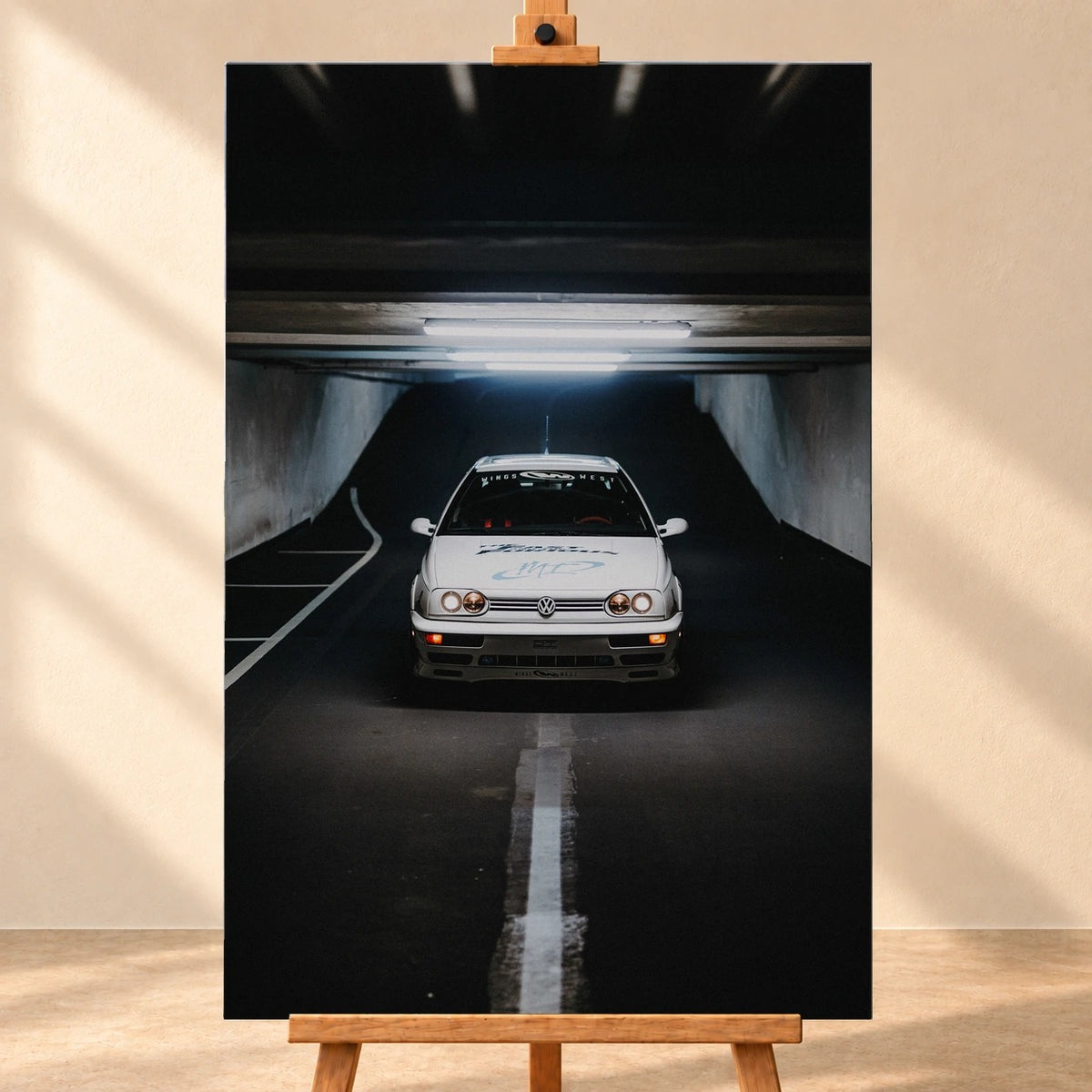 Visualisierung eines hochformatigen Leinwandbilds, frontal auf einer Holzstaffelei vor heller Wand. Das Motiv zeigt Jesses weißen VW Jetta aus „The Fast and the Furious“ von vorn unter Leuchtstoffröhren in einer dunklen Tiefgarage.