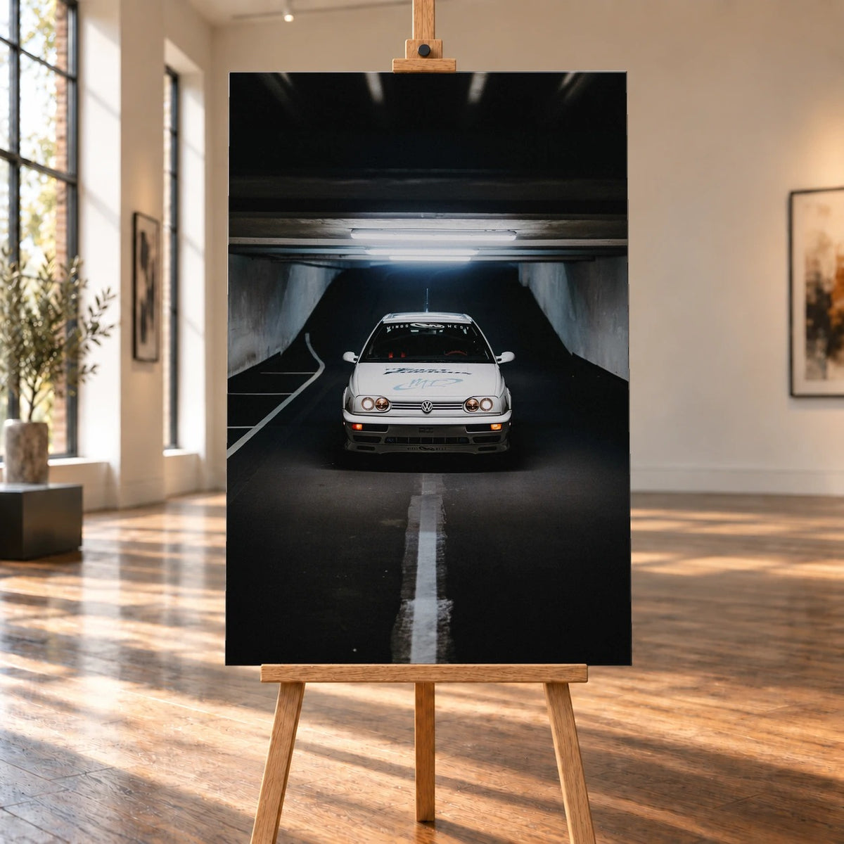 Raumvisualisierung mit einem hochformatigen Leinwandbild auf einer Holzstaffelei zwischen großen Fenstern und sonnigem Holzboden. Zu sehen ist Jesses weißer VW Jetta aus „The Fast and the Furious“ unter den Deckenleuchten einer dunklen Tiefgarage.