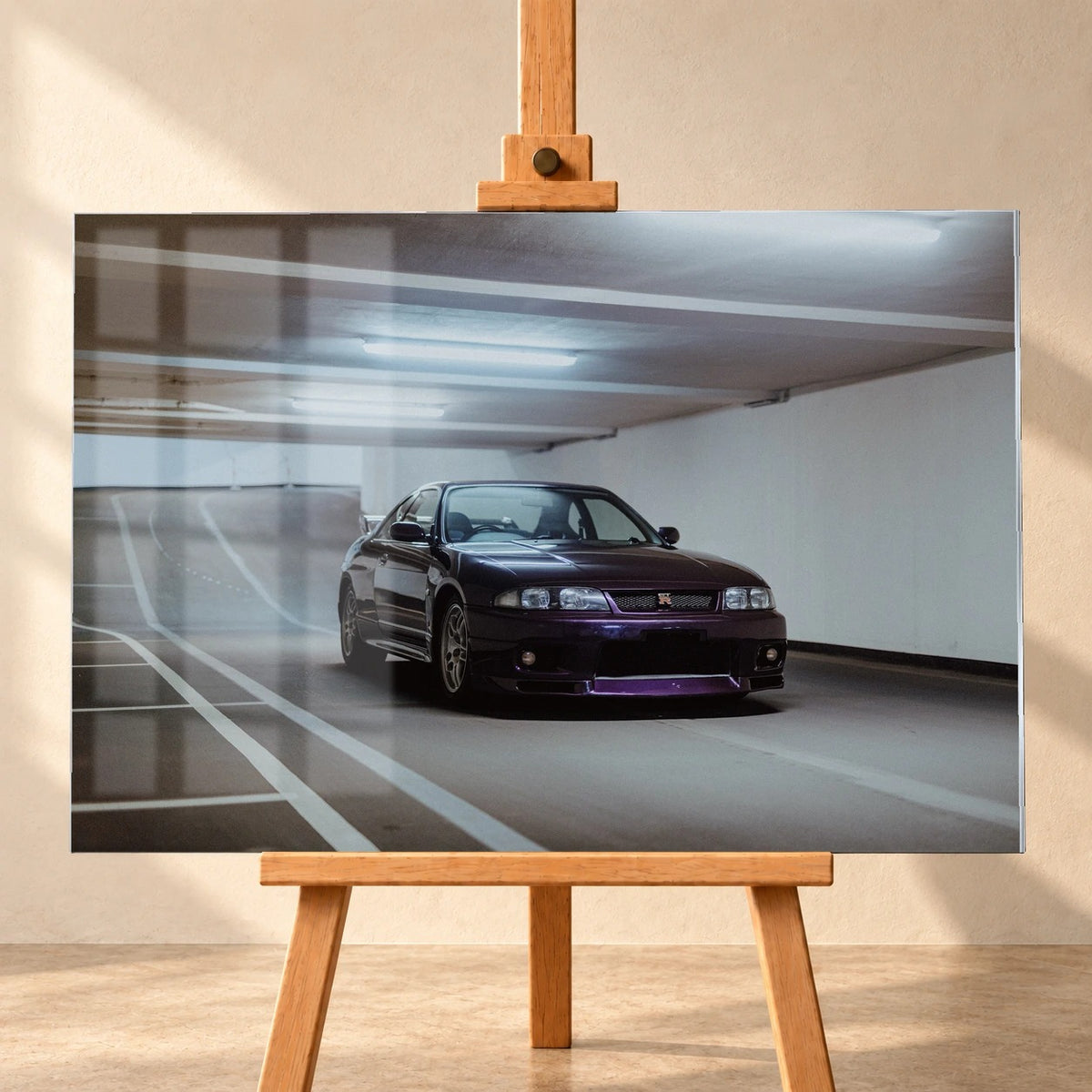 Visualisierung eines Acrylglasbilds im Querformat, frontal auf einer Holzstaffelei vor einer hellen Wand. Fensterreflexionen überlagern links das Motiv eines dunkelvioletten Nissan Skyline GT-R R33 in einer Tiefgarage.