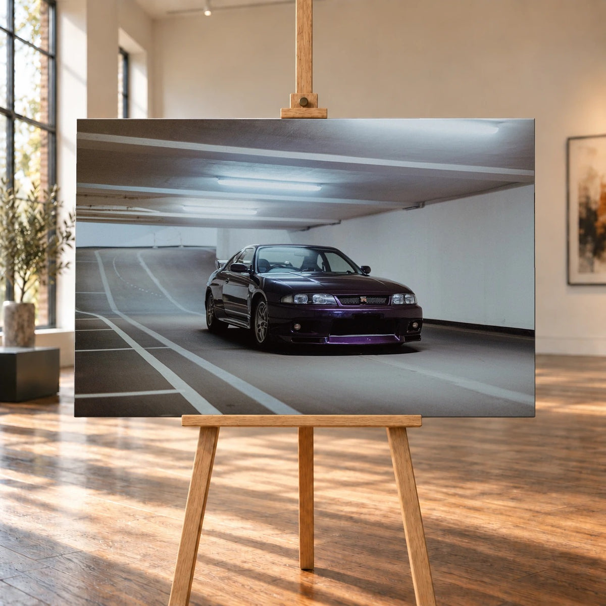 Raumvisualisierung eines querformatigen Leinwandbilds auf einer Holzstaffelei in einem hellen Raum mit hohen Fenstern und Holzboden. Das Automotiv zeigt einen dunkelvioletten Nissan Skyline GT-R R33 in Front-Dreiviertelansicht in einer Tiefgarage.