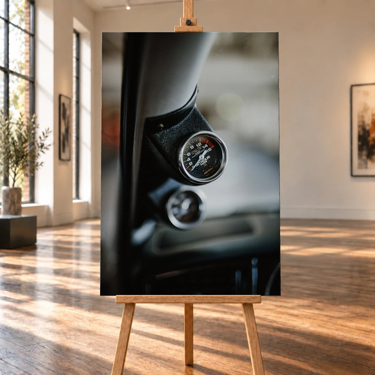 Raumvisualisierung eines hochformatigen Leinwandbilds auf einer Holzstaffelei in einem hellen Raum mit großen Fenstern und Holzboden. Das Bild zeigt eine Nahaufnahme der Lachgas-Druckanzeige in Jesse’s VW Jetta.