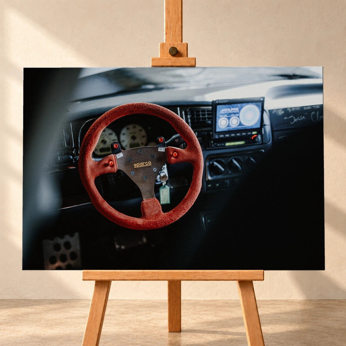 Visualisierung eines Leinwandbildes im Querformat auf einer Holzstaffelei vor heller Wand. Das Cockpit von Jesses VW Jetta aus „The Fast and the Furious“ zeigt ein rotes Sparco-Lenkrad und einen blauen Bildschirm.