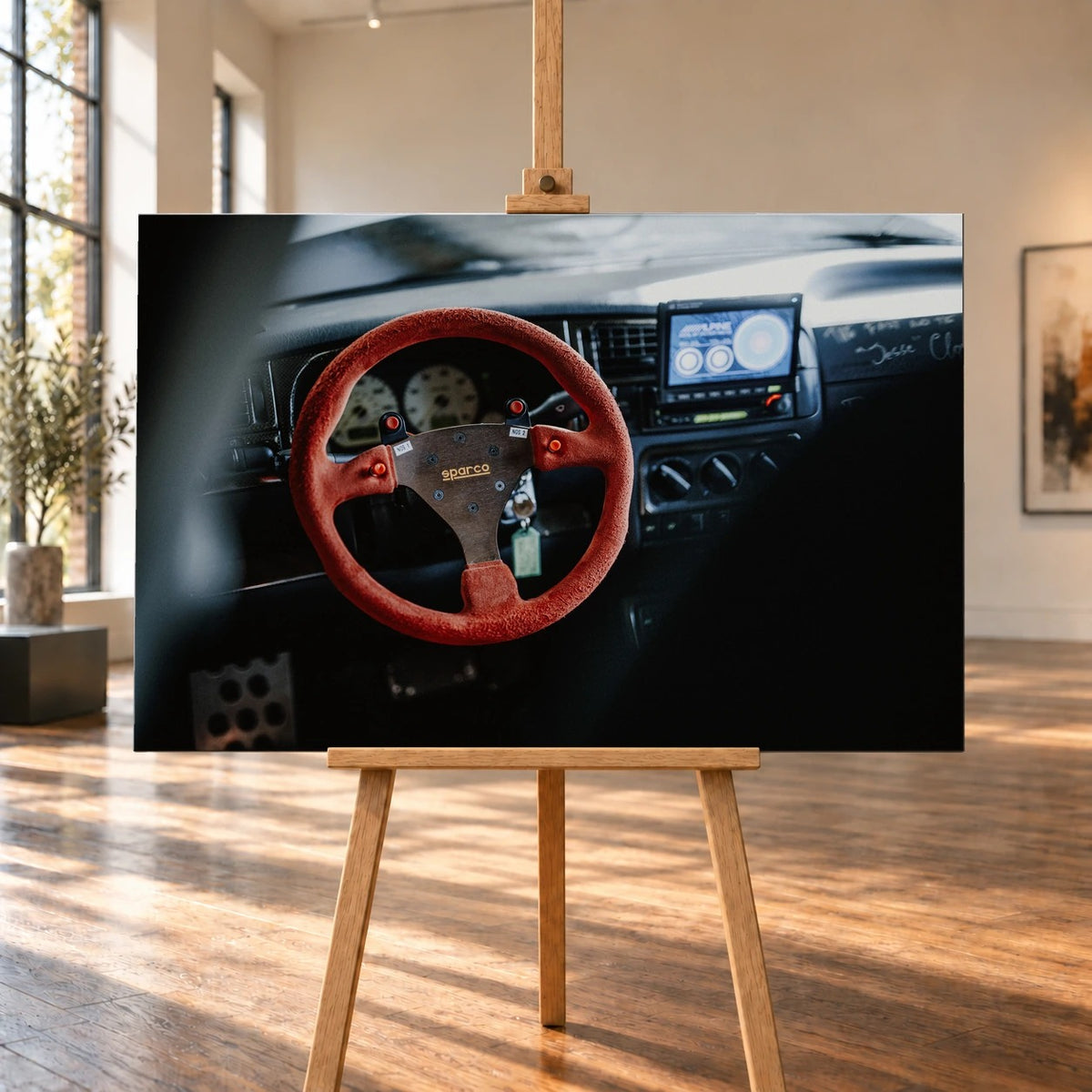 In einer Raumvisualisierung steht das querformatige Leinwandbild auf einer Holzstaffelei zwischen großen Fenstern und sonnenbeschienenem Holzboden. Es zeigt Jesses VW-Jetta-Cockpit aus „The Fast and the Furious“ mit rotem Sparco-Lenkrad.