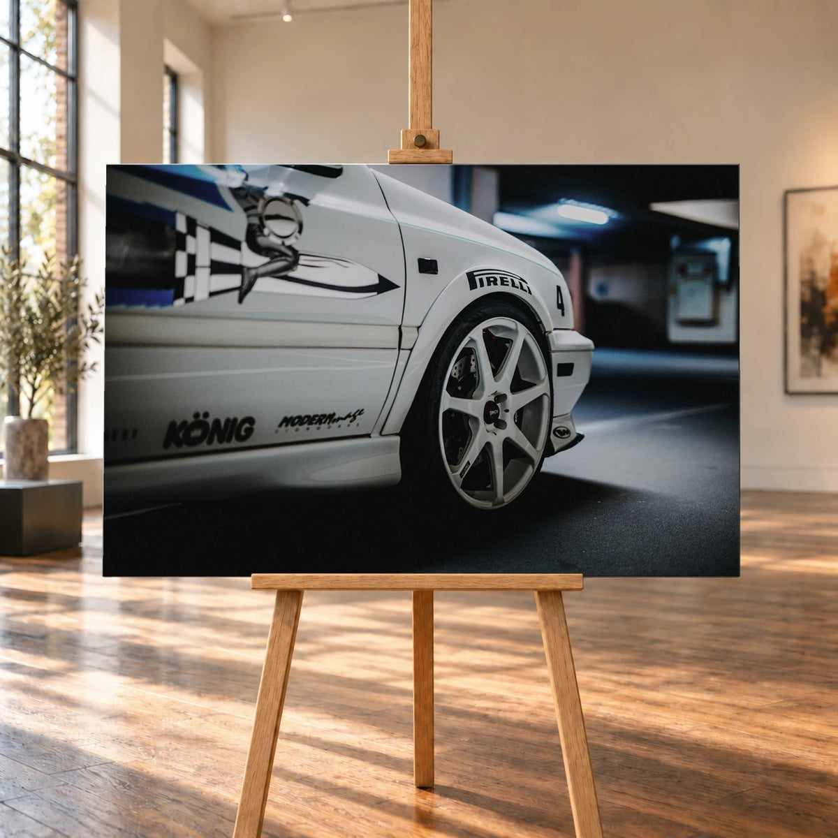 Raumvisualisierung mit einem querformatigen Leinwandbild auf einer Holzstaffelei in einem hellen Raum mit hohen Fenstern und Holzboden. Die Nahaufnahme von Jesses weißem VW Jetta aus „The Fast and the Furious“ rückt das Vorderrad und die grafisch beklebte Fahrzeugseite in den Mittelpunkt.