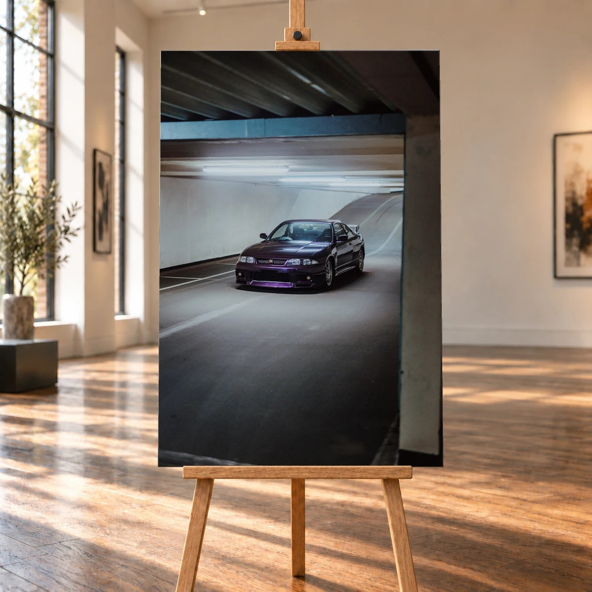 Raumvisualisierung eines hochformatigen Leinwandbildes auf einer Holzstaffelei in einem hellen Raum mit großen Fenstern und Holzboden. Das Bild zeigt einen dunkelvioletten Nissan Skyline GT-R R33 in Front-Dreiviertelansicht auf einer Parkhausrampе.
