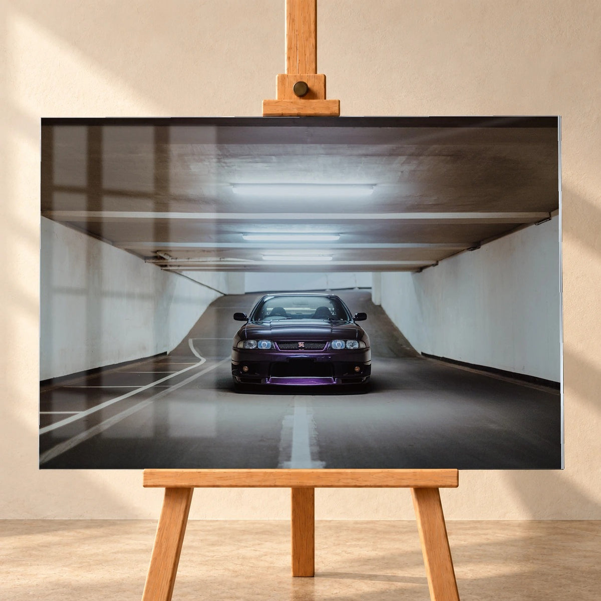 Visualisierung eines Acrylglasbildes im Querformat auf einer Holzstaffelei, frontal vor einer hellen Wand. Fensterspiegelungen liegen über dem Motiv eines dunkelvioletten Nissan Skyline GT-R R33 in einer Tiefgaragenzufahrt.