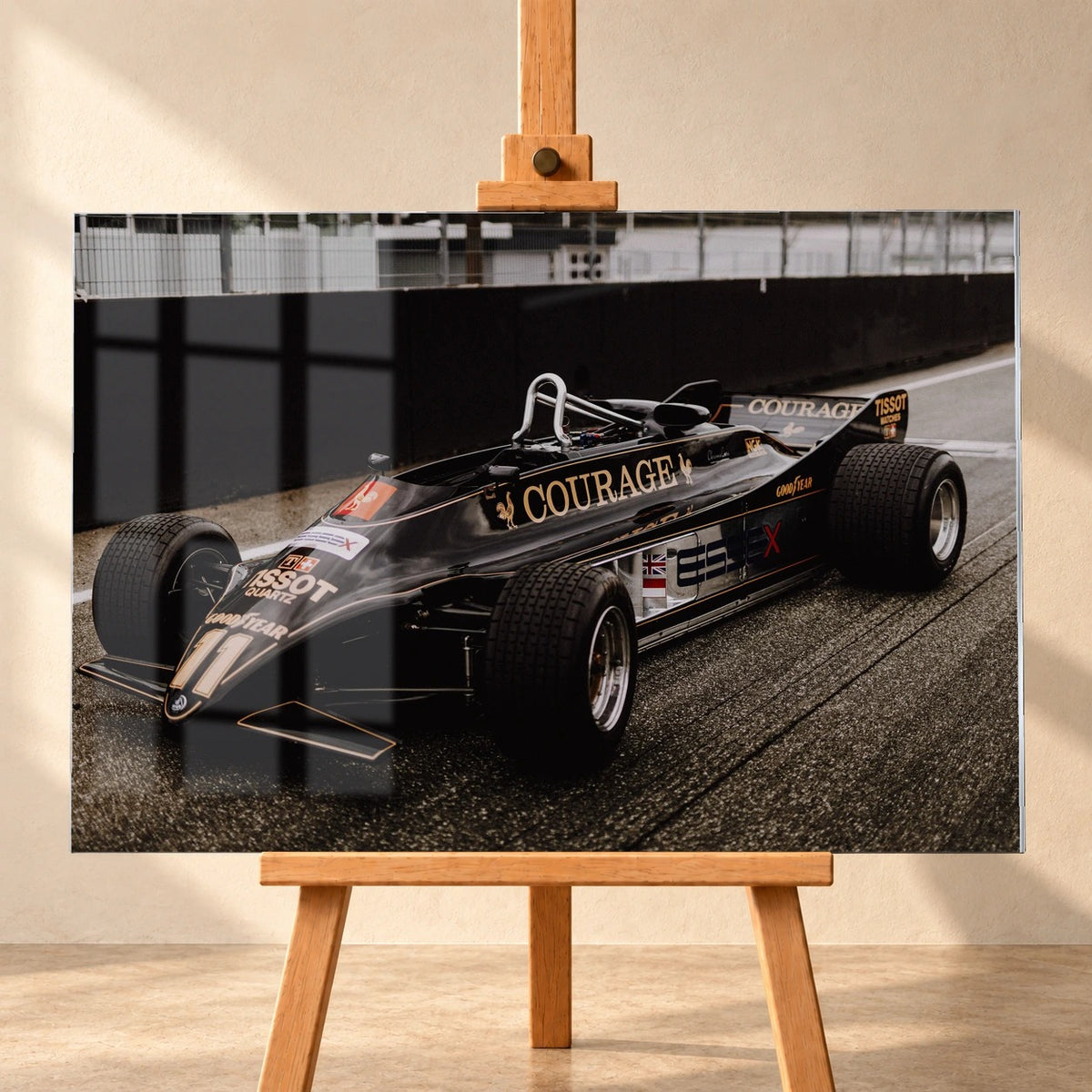 Visualisierung eines Acrylglasbilds im Querformat, frontal auf einer Holzstaffelei vor heller Wand. Der schwarze Lotus 88 mit goldenen Zierlinien und Startnummer 11 ist schräg von vorn zu sehen; eine Fensterspiegelung überlagert die linke Bildhälfte.