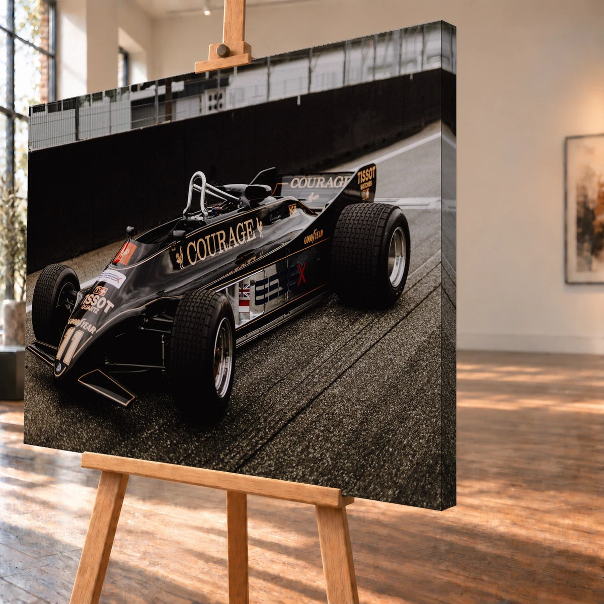 Schrägansicht des Leinwandbilds als Visualisierung auf einer Holzstaffelei, mit sichtbarer Tiefe und bedruckter rechter Seitenkante. Auf dem Motiv steht der schwarz-goldene Lotus 88 mit offenem Cockpit und Startnummer 11 vor einer dunklen Streckenbegrenzung.