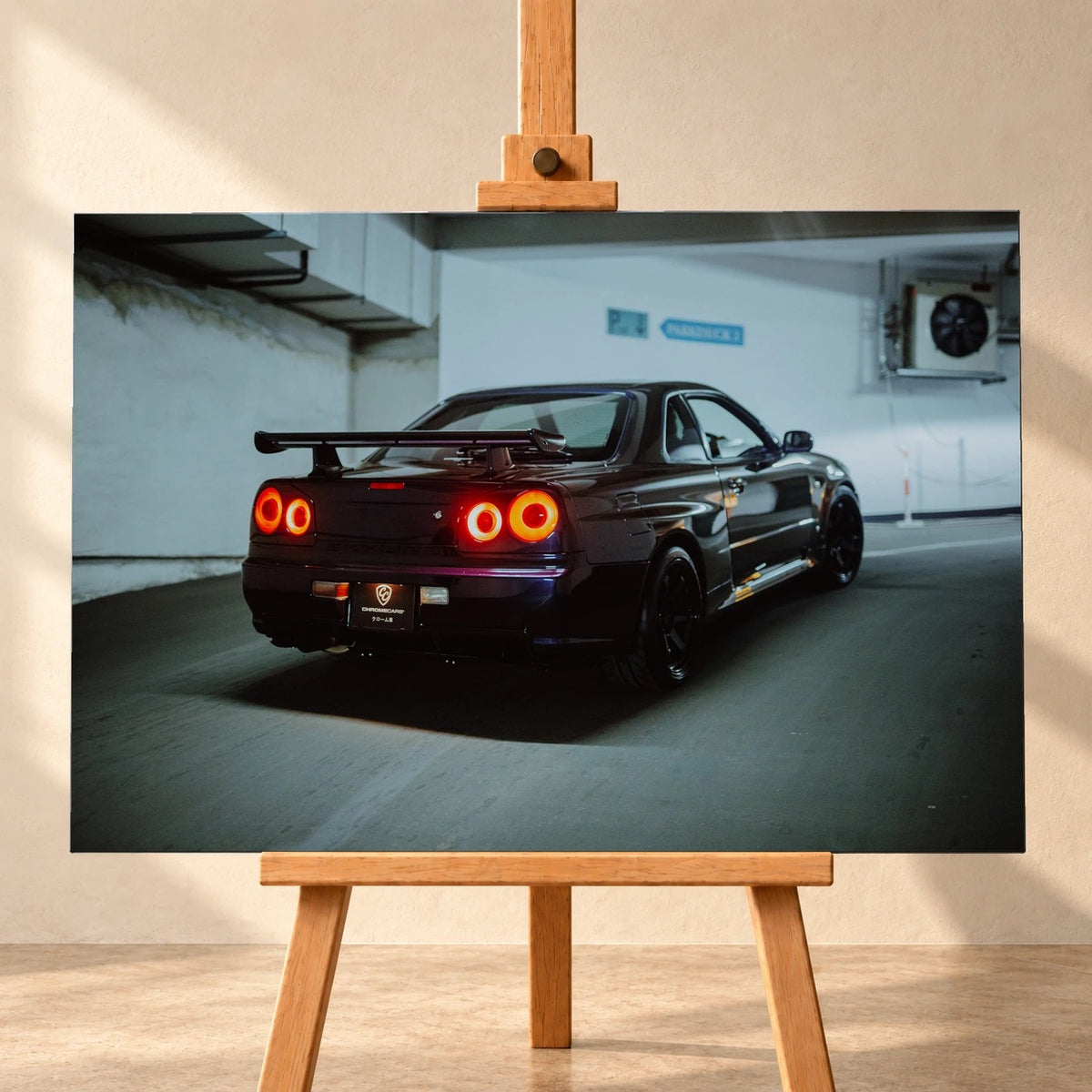 Frontale Visualisierung eines Leinwandbilds im Querformat auf einer Holzstaffelei vor einer hellen Wand. Das Motiv zeigt einen dunkelvioletten Nissan Skyline R34 schräg von hinten in einer Tiefgarage, mit großem Heckflügel und vier leuchtenden runden Rücklichtern.