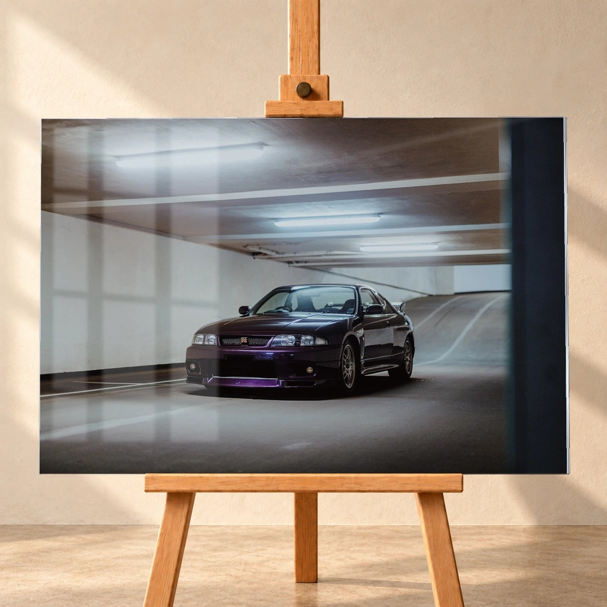 Visualisierung eines Acrylglas-Wandbilds, frontal auf einer Holzstaffelei vor heller Wand präsentiert. Fensterreflexionen liegen über dem Motiv eines dunkelvioletten Nissan Skyline GT-R R33, der schräg von vorn in einer Tiefgarage zu sehen ist.
