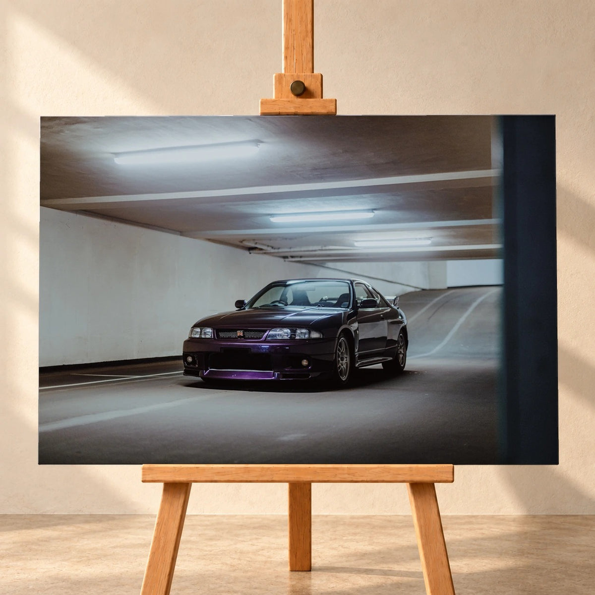 Frontale Visualisierung eines querformatigen Leinwandbilds auf einer Holzstaffelei vor heller Wand. Das Motiv zeigt einen dunkelvioletten Nissan Skyline GT-R R33 schräg von vorn in einer Tiefgarage unter Leuchtstoffröhren.