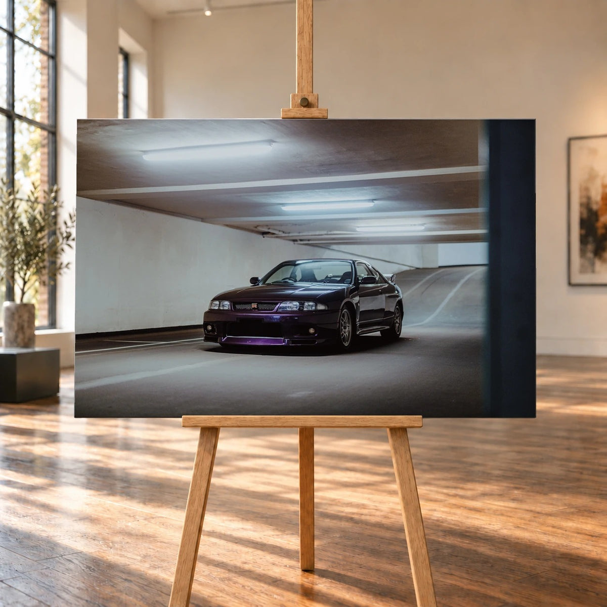 Raumvisualisierung mit einem querformatigen Leinwandbild auf einer Holzstaffelei in einem hellen Raum mit großen Fenstern und Holzboden. Zu sehen ist ein dunkelvioletter Nissan Skyline GT-R R33 in Frontschrägansicht in einer Tiefgarage.