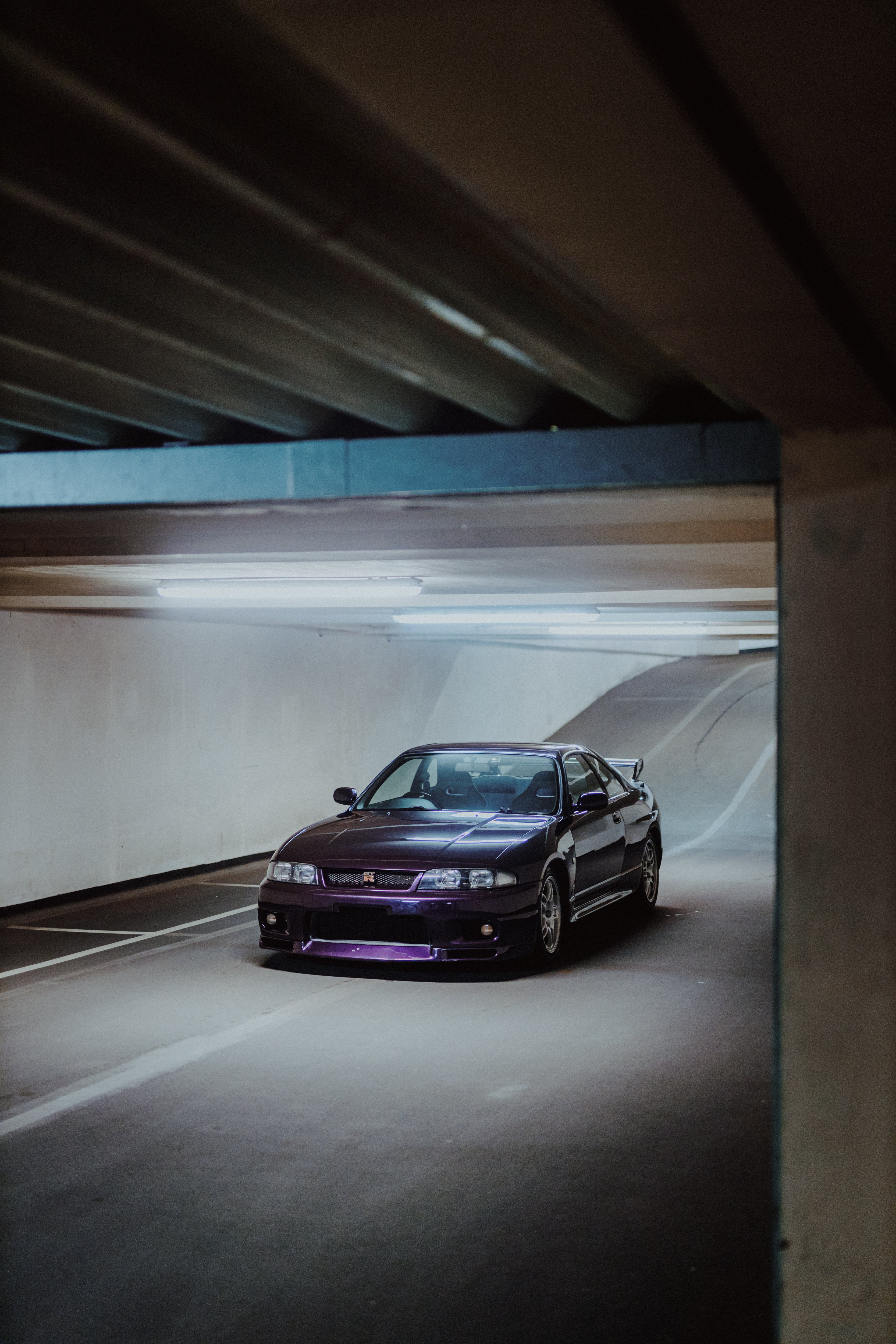 Dunkelvioletter Nissan Skyline R33 GT-R NMP1 schräg von vorn in einer Tiefgarage mit viel freiem Raum um das Fahrzeug.