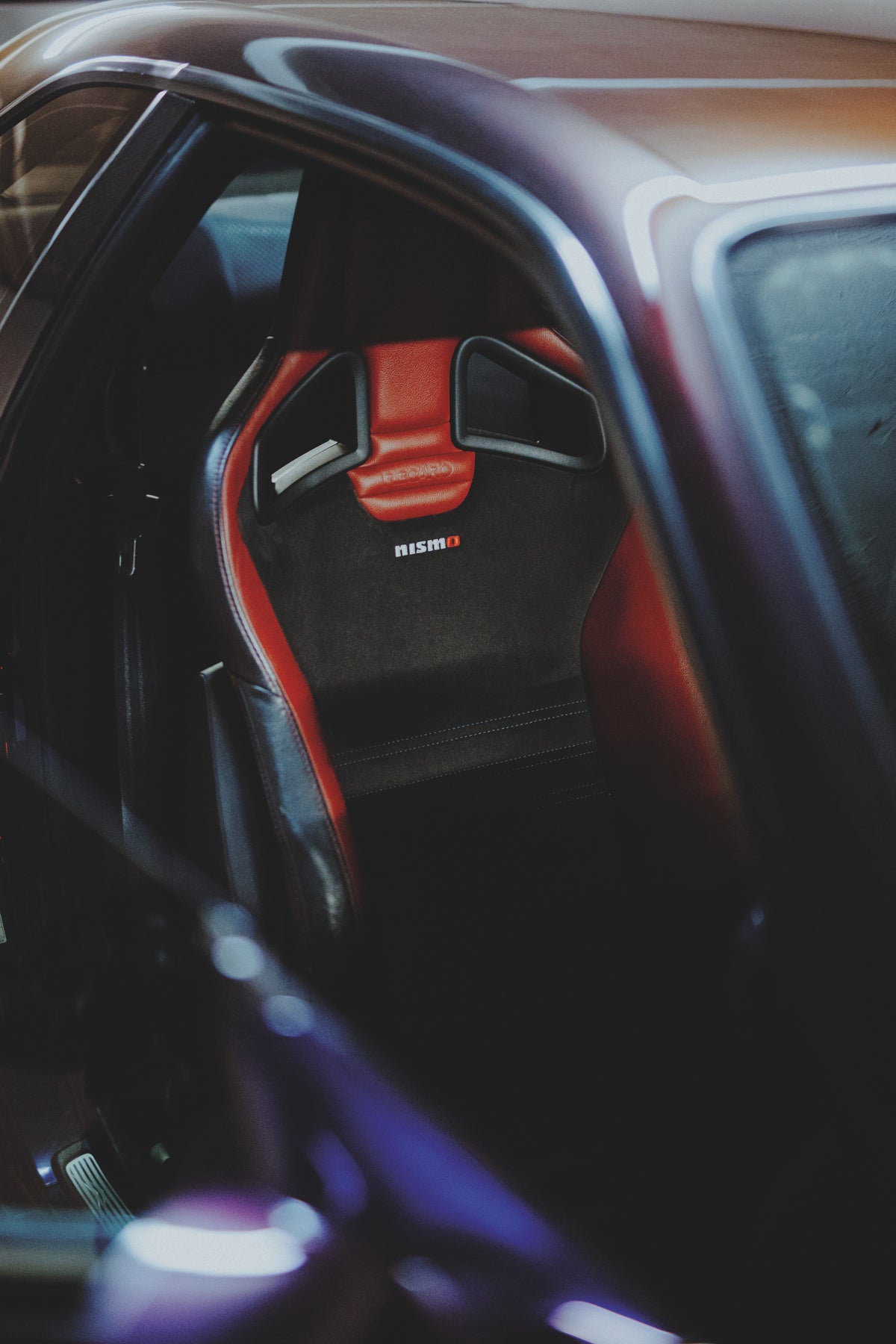 Blick durch die geöffnete Tür eines Nissan Skyline R34 auf einen schwarz-roten Sportsitz.