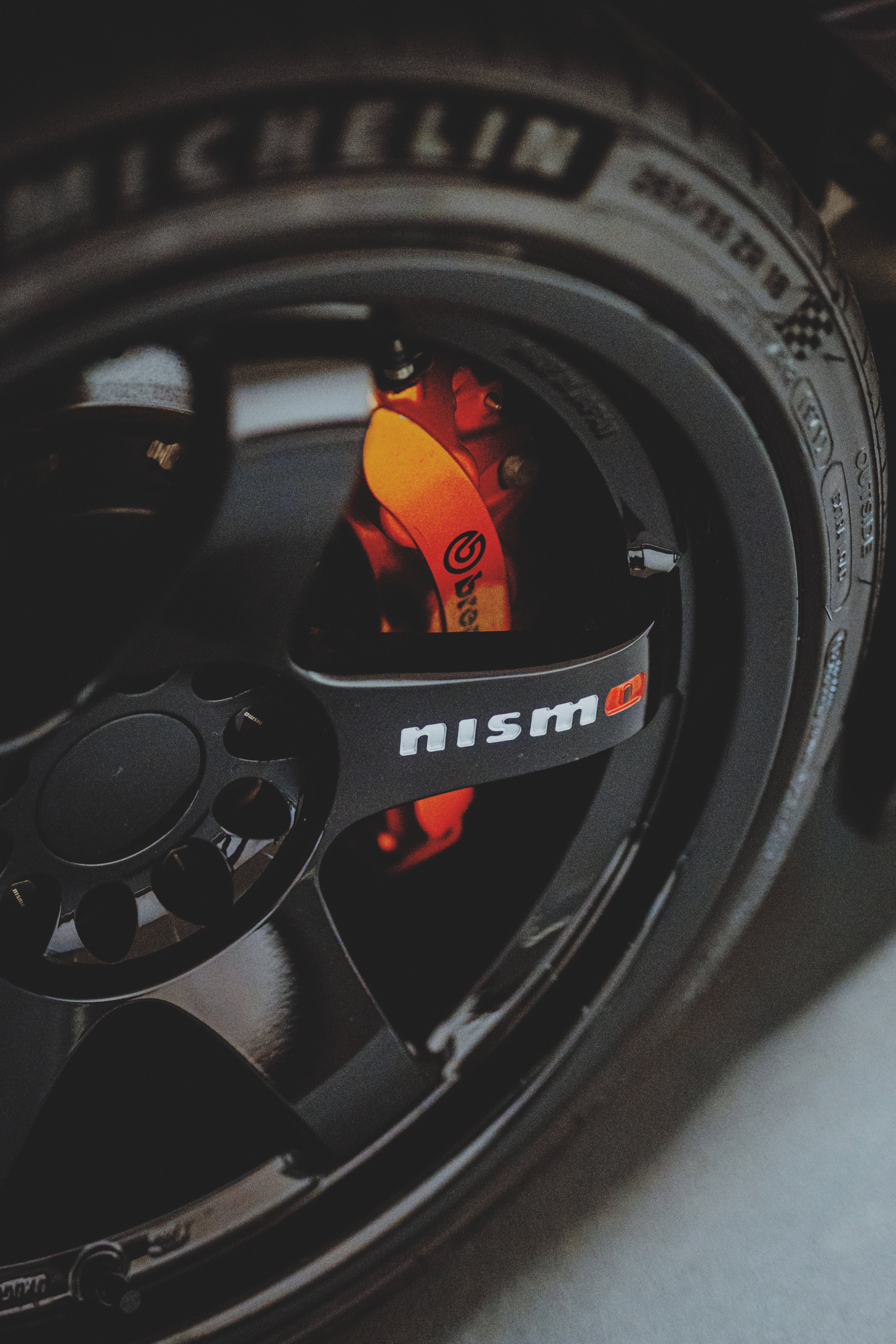Schwarze Felge mit Nismo-Schriftzug und orangefarbenem Bremssattel hinter den Speichen.