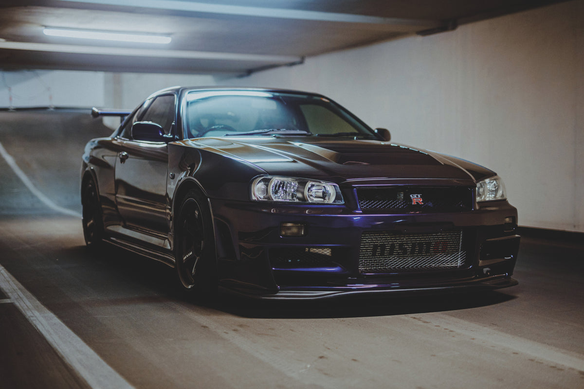 Nissan Skyline R34 schräg von vorn vor einer Garagenrampe, mit hellem Deckenlicht auf der Motorhaube.