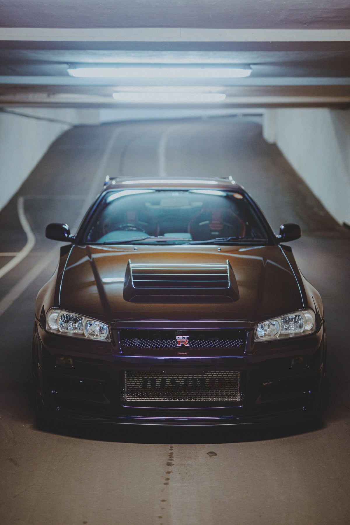 Nissan Skyline R34 von erhöhtem Standpunkt frontal in einer Tiefgarage, mit deutlich sichtbarer Motorhaube.