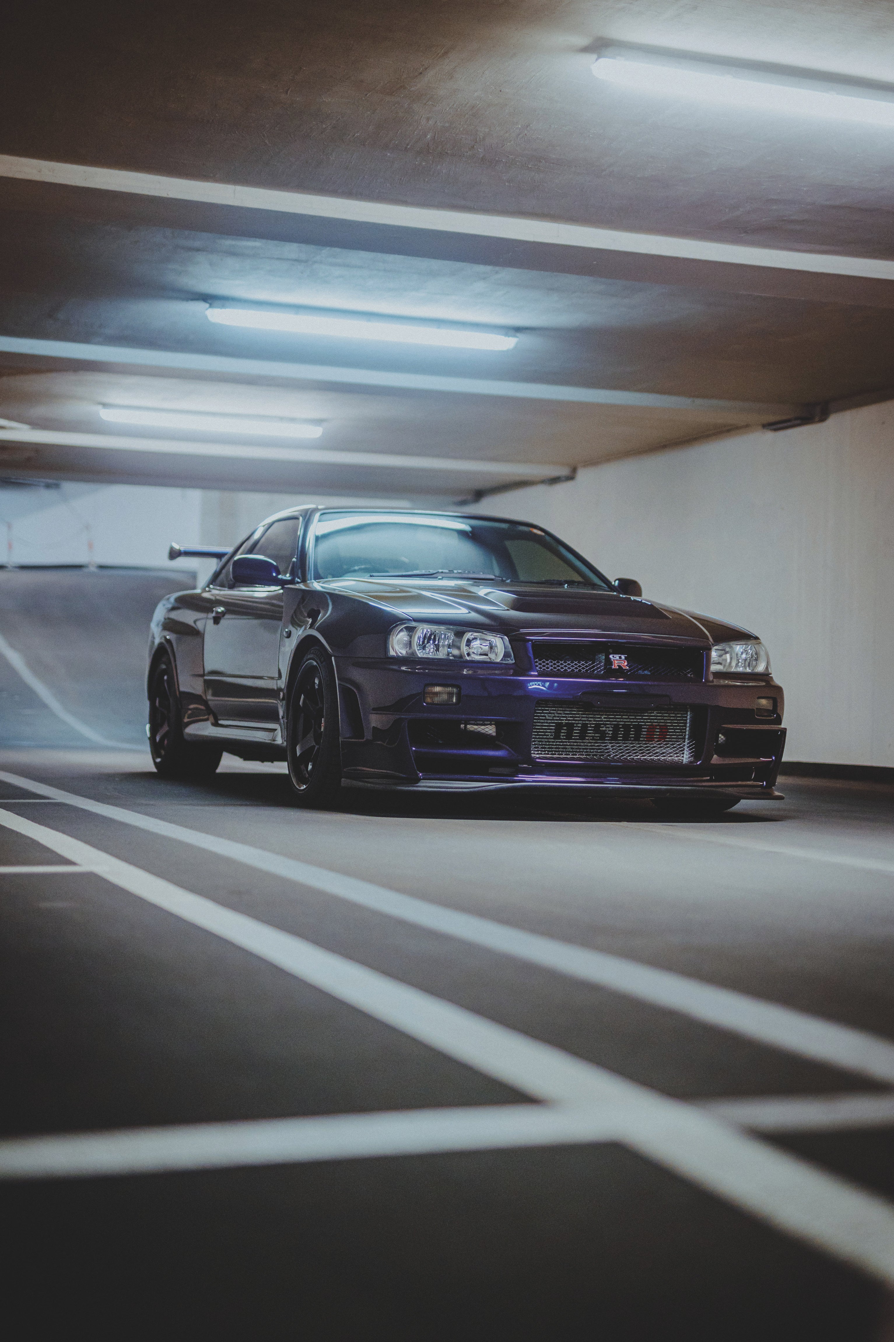 Nissan Skyline R34 schräg von vorn hinter weißen schrägen Bodenmarkierungen in einer Tiefgarage.