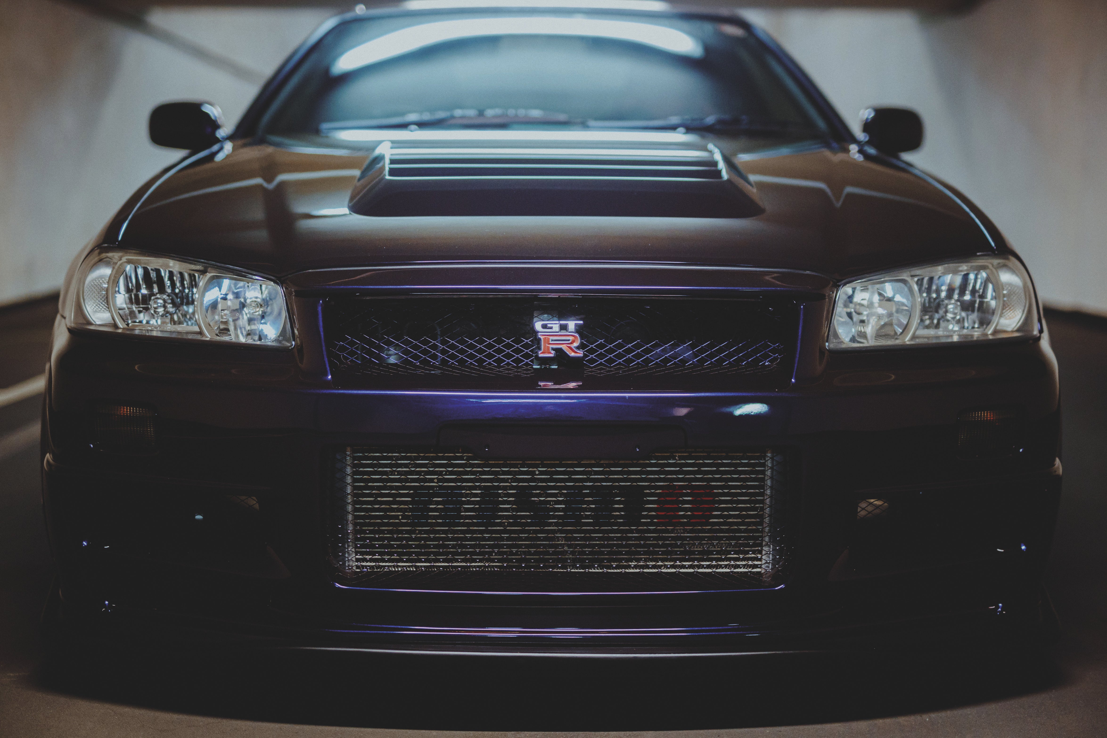 Frontale Nahansicht eines Nissan Skyline R34 mit Scheinwerfern, GT-R-Emblem und geformter Motorhaube.