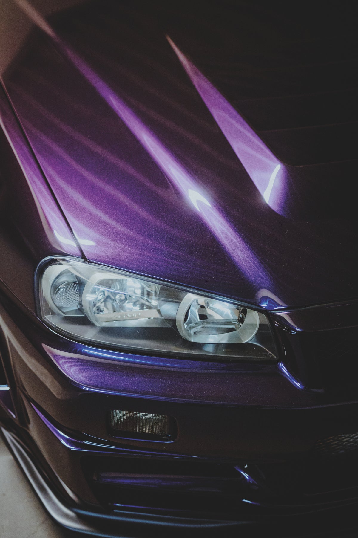Nahaufnahme von Scheinwerfer, Stoßfänger und violett reflektierender Motorhaube eines Nissan Skyline R34.