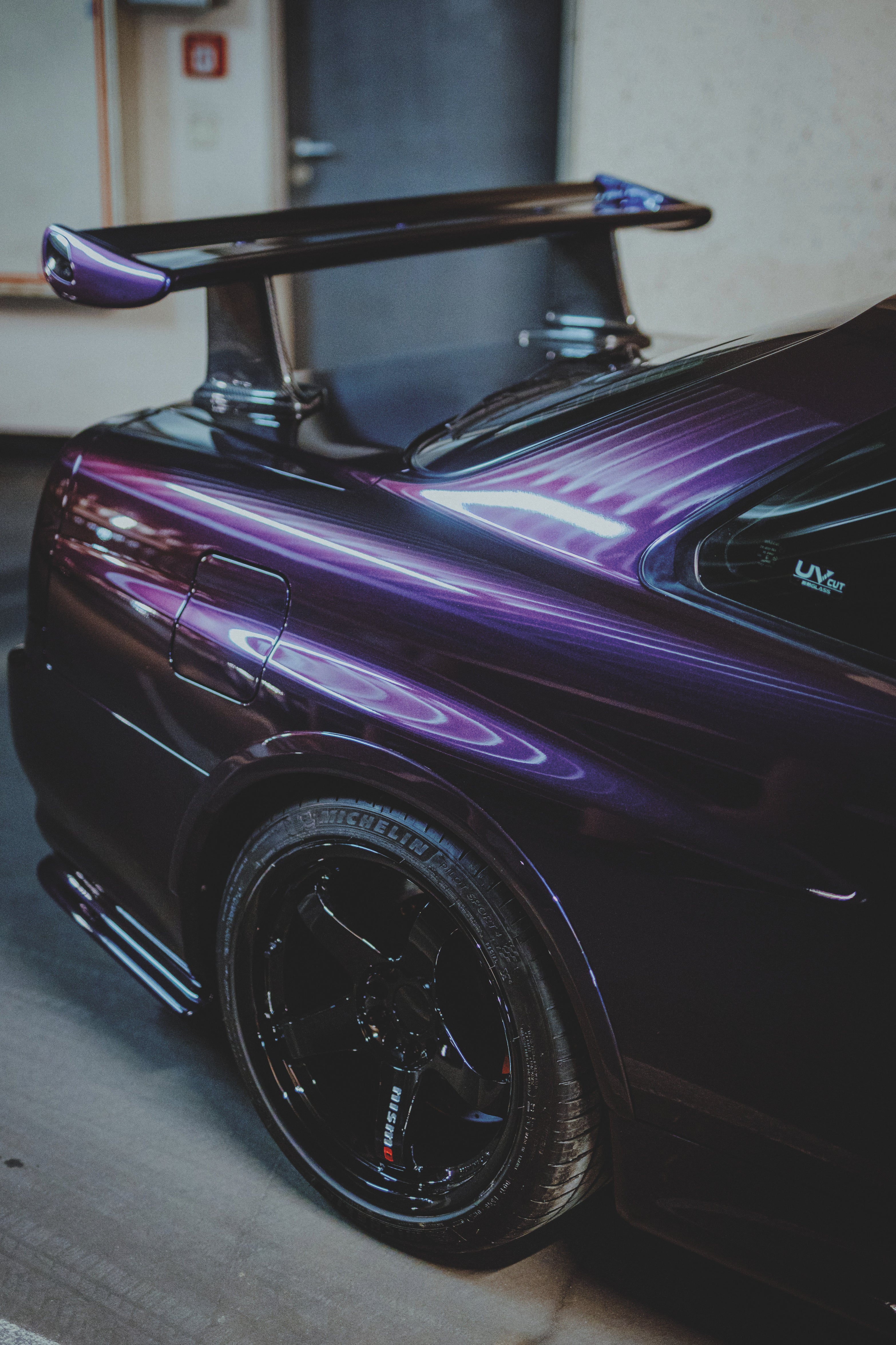 Nahansicht des violetten hinteren Seitenteils eines Nissan Skyline R34 mit schwarzem Rad und Heckflügel.