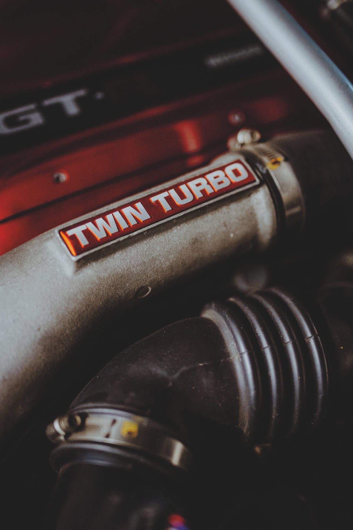 Motorraumdetail mit rotem Bauteil, silbernem Rohr mit Twin-Turbo-Schriftzug und schwarzem Schlauch.