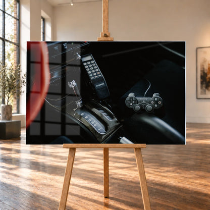 Die dunkle Cockpitaufnahme konzentriert sich auf Automatik-Wählhebel, Bedieneinheit und PlayStation-Controller. Motiv „Night Light“ als Acrylglas-Wandbild, auf einer Holzstaffelei in einem hellen Galerieraum.