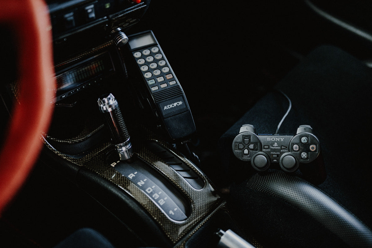 Die dunkle Cockpitaufnahme konzentriert sich auf Automatik-Wählhebel, Bedieneinheit und PlayStation-Controller. Originalmotiv „Night Light“ im Querformat.