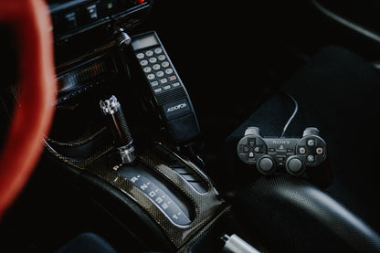 Die dunkle Cockpitaufnahme konzentriert sich auf Automatik-Wählhebel, Bedieneinheit und PlayStation-Controller. Originalmotiv „Night Light“ im Querformat.
