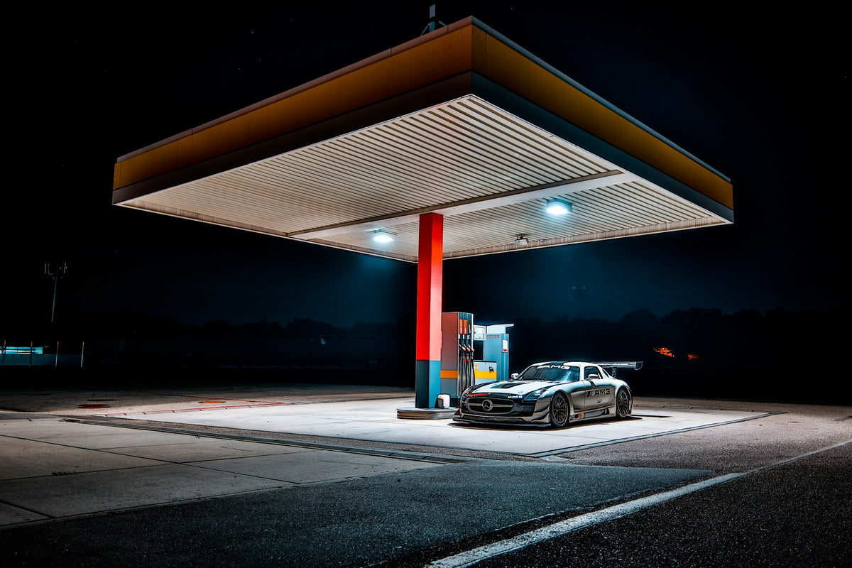 Der Mercedes SLS GT3 steht nachts allein unter dem Lichtdach einer Tankstelle; Rot, Blau und Orange gliedern die dunkle Szene. Originalmotiv „Apex Scene“ im Querformat.