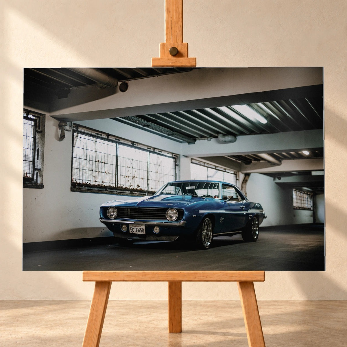 Der Camaro Yenko steht schräg von vorn in einer alten, lichtdurchfluteten Halle; Fensterreihen und Beton schaffen industrielle Atmosphäre. Motiv „Silver Pulse 2“ als Alu gebürstet-Wandbild, frontal auf einer Holzstaffelei.