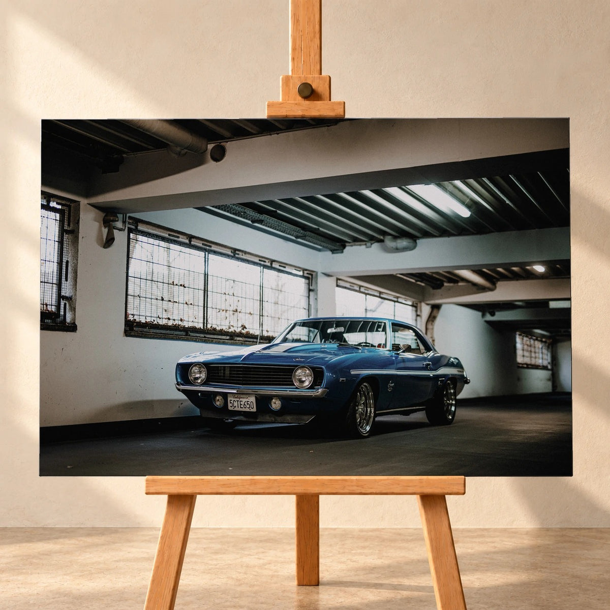 Der Camaro Yenko steht schräg von vorn in einer alten, lichtdurchfluteten Halle; Fensterreihen und Beton schaffen industrielle Atmosphäre. Motiv „Silver Pulse 2“ als Leinwand-Wandbild, frontal auf einer Holzstaffelei.