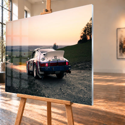 Der Porsche 911 Safari steht von hinten auf einer Anhöhe im Abendrot; weiter Himmel und orangefarbene Horizontlinie öffnen das Bild. Motiv „Fast Motion“ als Acrylglas-Wandbild, schräg von der Seite auf einer Holzstaffelei.