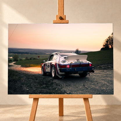 Der Porsche 911 Safari steht von hinten auf einer Anhöhe im Abendrot; weiter Himmel und orangefarbene Horizontlinie öffnen das Bild. Motiv „Fast Motion“ als Leinwand-Wandbild, frontal auf einer Holzstaffelei.