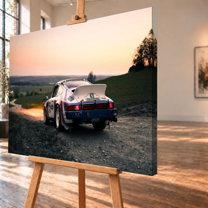 Der Porsche 911 Safari steht von hinten auf einer Anhöhe im Abendrot; weiter Himmel und orangefarbene Horizontlinie öffnen das Bild. Motiv „Fast Motion“ als Leinwand-Wandbild, schräg von der Seite auf einer Holzstaffelei.