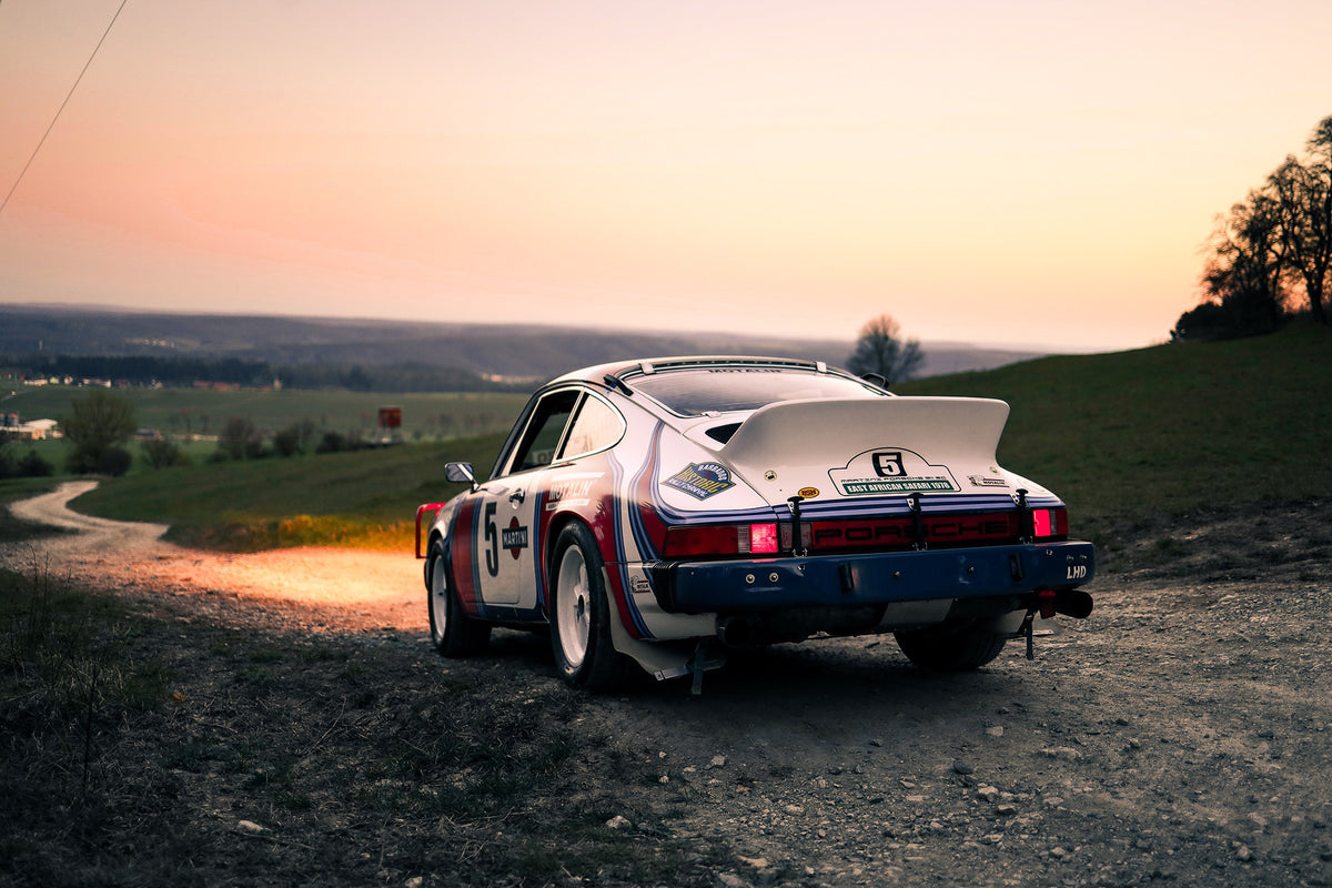 Der Porsche 911 Safari steht von hinten auf einer Anhöhe im Abendrot; weiter Himmel und orangefarbene Horizontlinie öffnen das Bild. Originalmotiv „Fast Motion“ im Querformat.