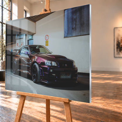 Dunkelvioletter Nissan Skyline R34 in einem Parkhaus, schräg von vorn fotografiert, mit schwarzen Rädern, großem Heckflügel und pink-violetten Lichtreflexionen auf der Karosserie; Visualisierung als Acrylglas-Wandbild, schräg von der Seite auf einer Holzstaffelei.