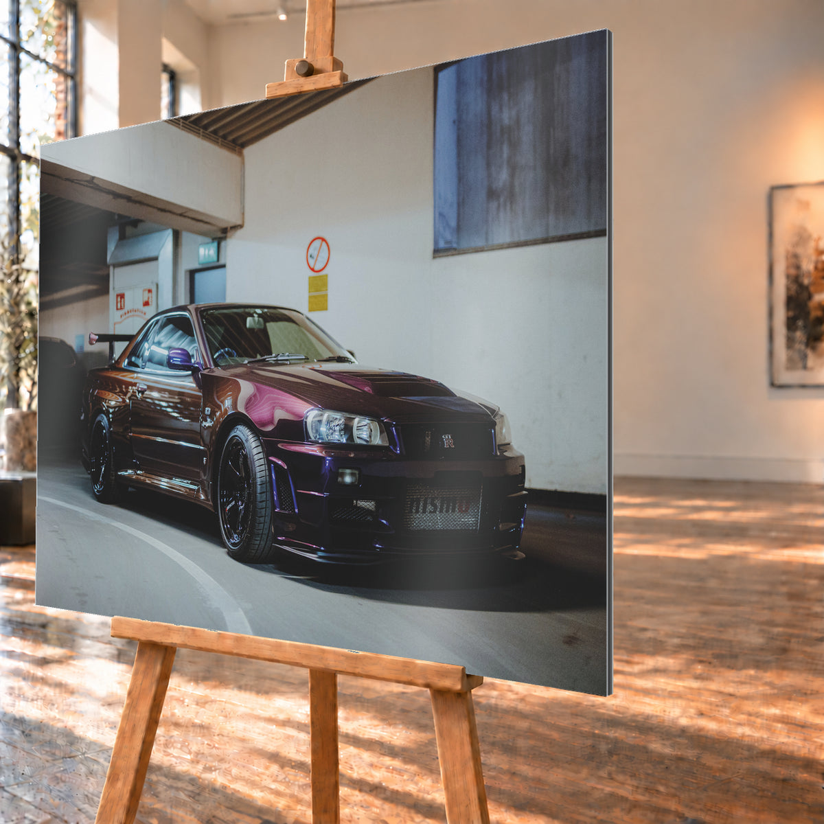 Dunkelvioletter Nissan Skyline R34 in einem Parkhaus, schräg von vorn fotografiert, mit schwarzen Rädern, großem Heckflügel und pink-violetten Lichtreflexionen auf der Karosserie; Visualisierung als Alu gebürstet-Wandbild, schräg von der Seite auf einer Holzstaffelei.