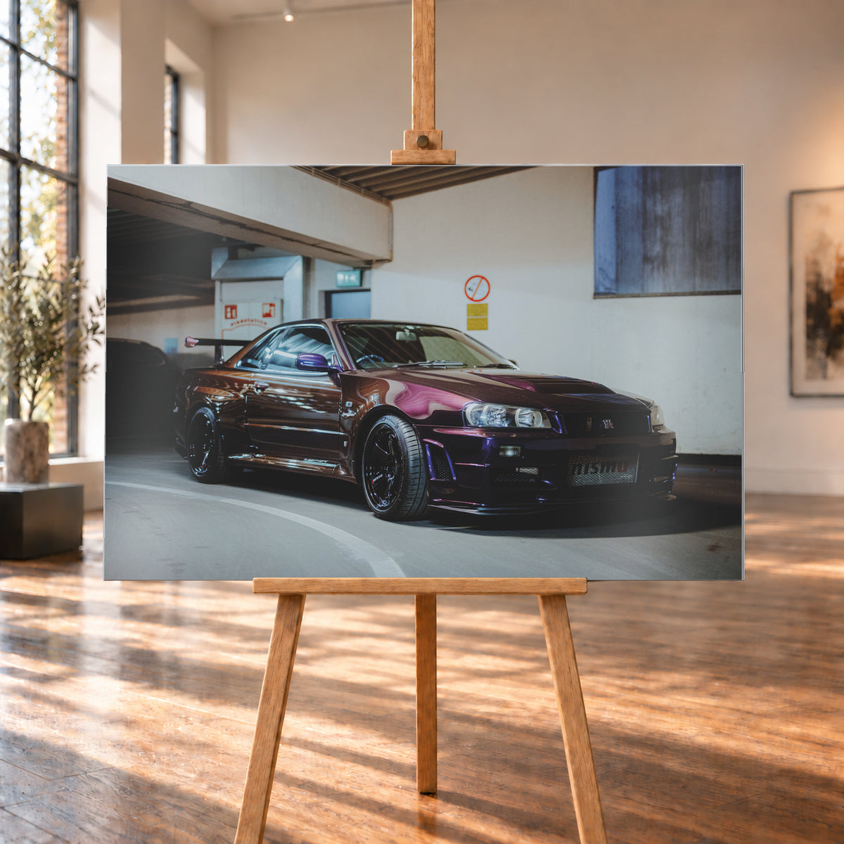Dunkelvioletter Nissan Skyline R34 in einem Parkhaus, schräg von vorn fotografiert, mit schwarzen Rädern, großem Heckflügel und pink-violetten Lichtreflexionen auf der Karosserie; Visualisierung als Alu gebürstet-Wandbild, auf einer Holzstaffelei in einem hellen Galerieraum.