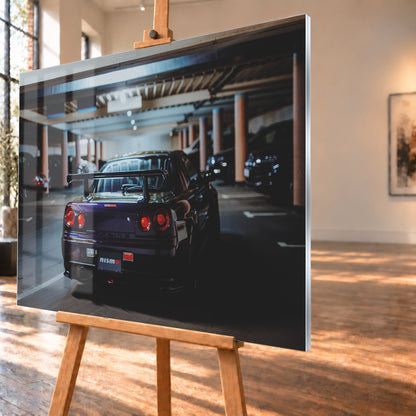 Heckansicht eines dunkelvioletten Nissan Skyline R34 mit großem Heckflügel und vier rot leuchtenden runden Rücklichtern auf einer überdachten Parkebene. Rötliche Säulen, Deckenbalken und unscharf abgestellte Fahrzeuge rahmen das Auto; kühles, gedämpftes Licht spiegelt sich auf der Karosserie; Visualisierung als Acrylglas-Wandbild, schräg von der Seite auf einer Holzstaffelei.