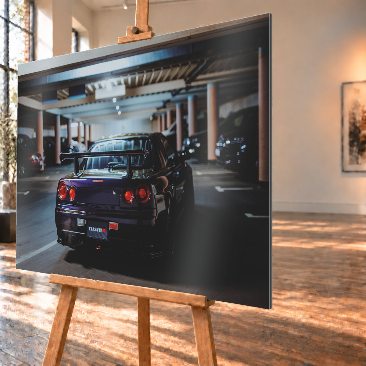 Heckansicht eines dunkelvioletten Nissan Skyline R34 mit großem Heckflügel und vier rot leuchtenden runden Rücklichtern auf einer überdachten Parkebene. Rötliche Säulen, Deckenbalken und unscharf abgestellte Fahrzeuge rahmen das Auto; kühles, gedämpftes Licht spiegelt sich auf der Karosserie; Visualisierung als Alu gebürstet-Wandbild, schräg von der Seite auf einer Holzstaffelei.