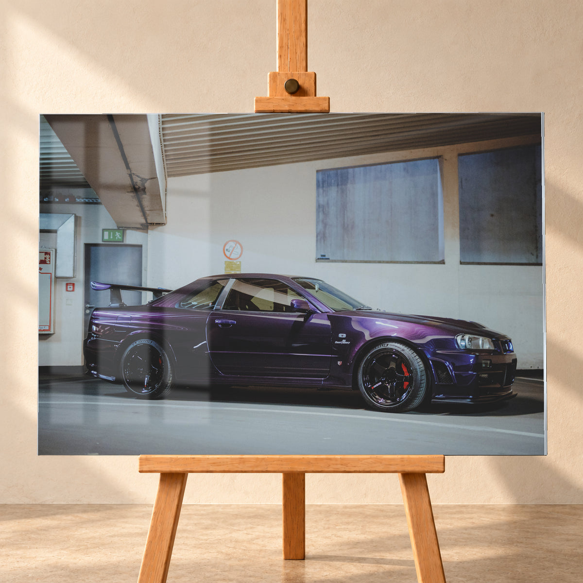 Violetter Nissan Skyline R34, nahezu seitlich mit der Front nach rechts, in einem hellen Parkgaragen-Innenraum; sichtbar sind schwarze Räder, rote Bremssättel und ein großer Heckflügel; Visualisierung als Acrylglas-Wandbild, frontal auf einer Holzstaffelei.